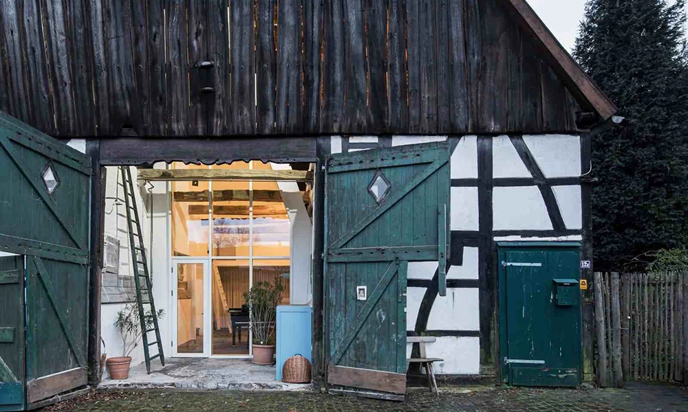 Das Bild zeigt die renovierte, verglaste Front des Dortmannshofs, einem historischen Fachwerkhaus mit großen, geöffneten Holztüren.