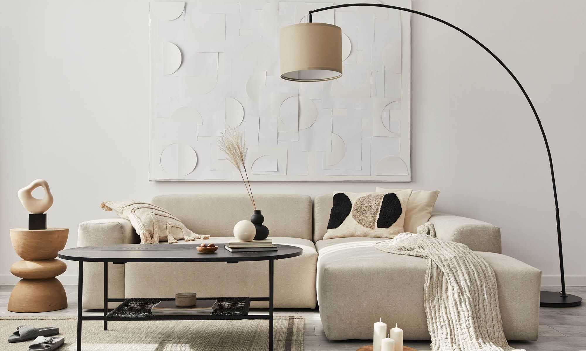 A chic living room with a beige sofa, black coffee table, artistic wall decor, and an arching floor lamp.
