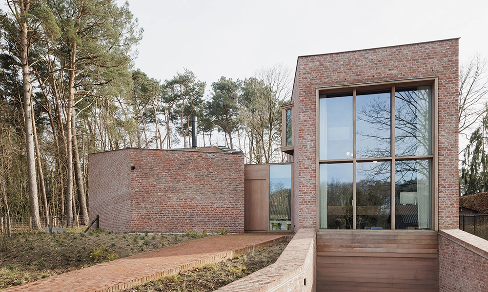 Ein modernes Gebäude mit roten Ziegelsteinen, großen Fensterflächen und minimalistischem Design, das von Bäumen umgeben ist und eine gepflasterte Einfahrt hat – ein Beispiel für eine gelungene Fassadensanierung.