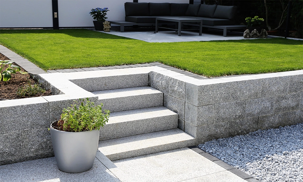 Eine Außentreppe aus Granit führt zu einem Garten mit Rasenfläche.