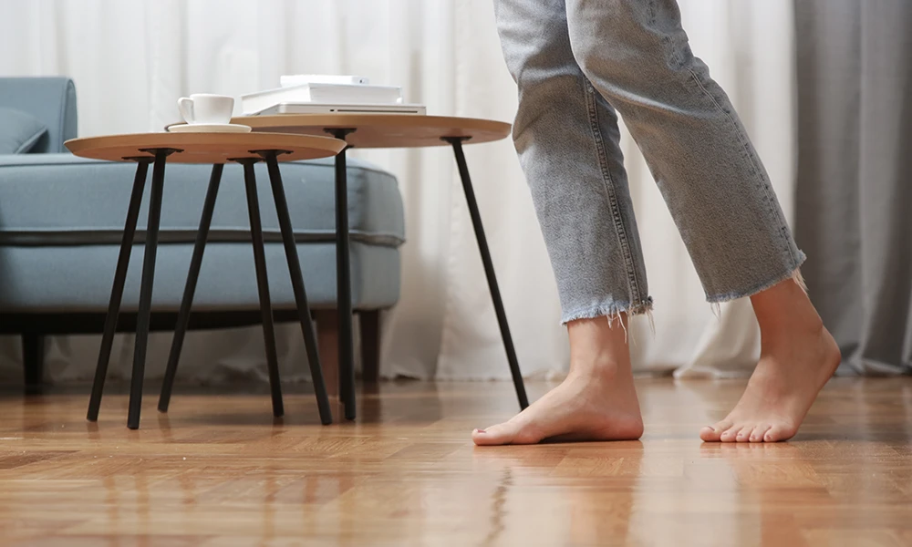 Die Füße einer Person in Jeans, die barfuß auf einem polierten Holzboden mit nachgerüsteter Fußbodenheizung im Altbau geht.