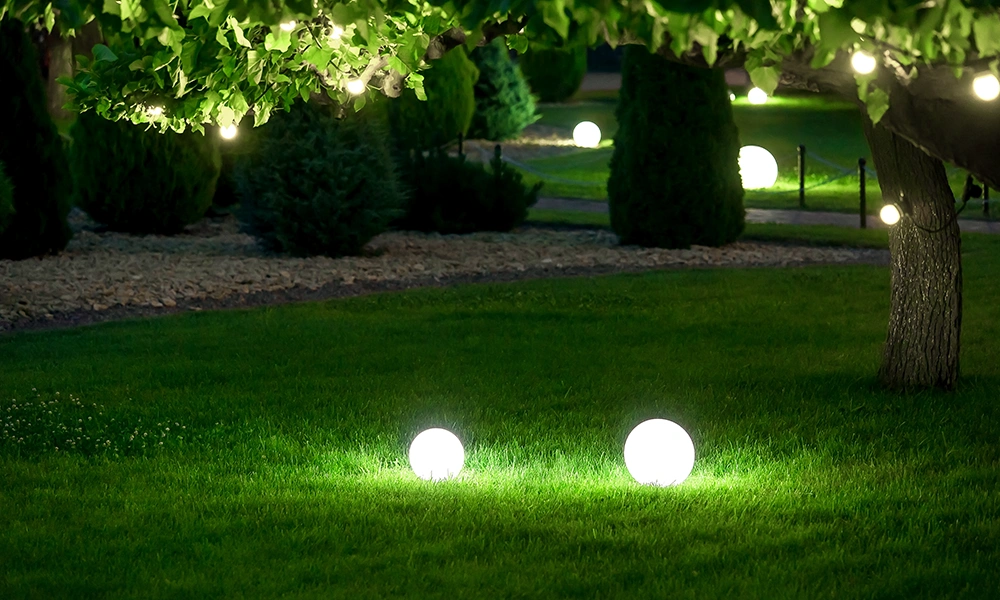 Nighttime garden with glowing spherical lights on the lawn and in trees.