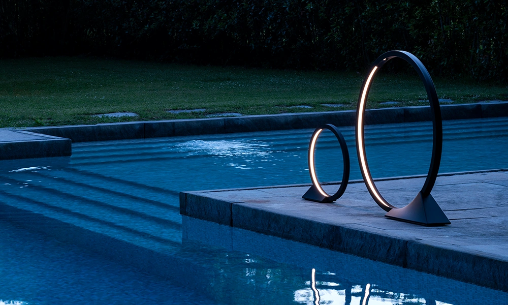 Two circular outdoor lamps beside a swimming pool at twilight.