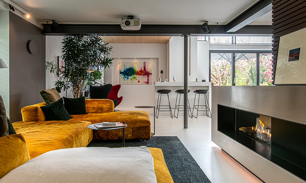 Ein modernisiertes Wohnzimmer eines 80er Jahre Hauses mit einem gemütlichen, gelben Sofa und einem modernen Kamin.