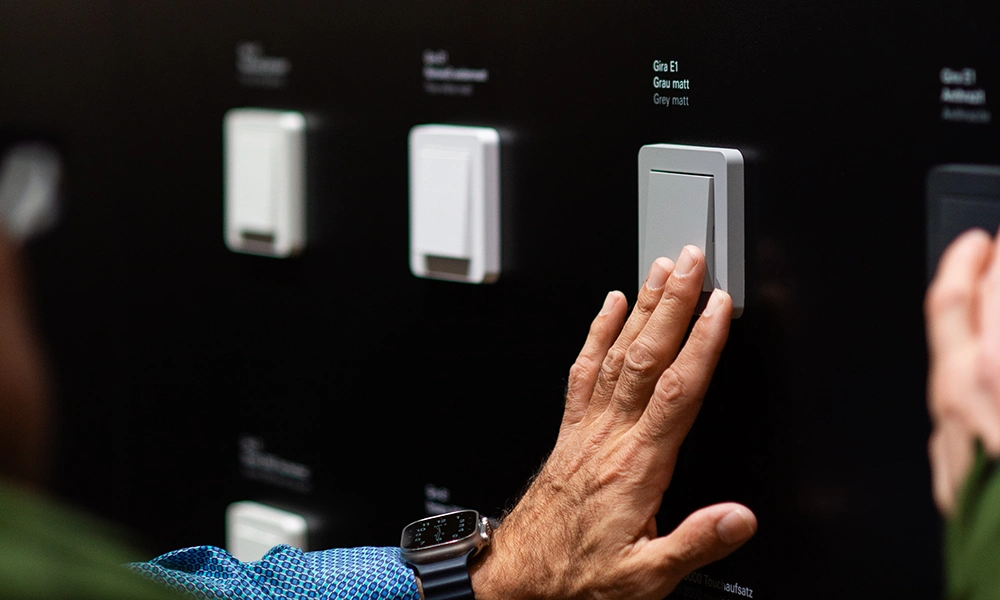 Person interacting with a display of various Gira E1 light switches in different colours and styles.