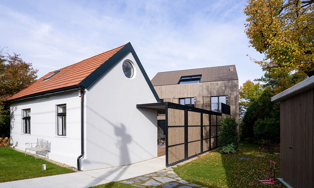 Ein saniertes 50er-Jahre-Haus mit einem modernen Anbau, der durch seine Holzfassade einen harmonischen Kontrast zum klassischen Putz bildet.