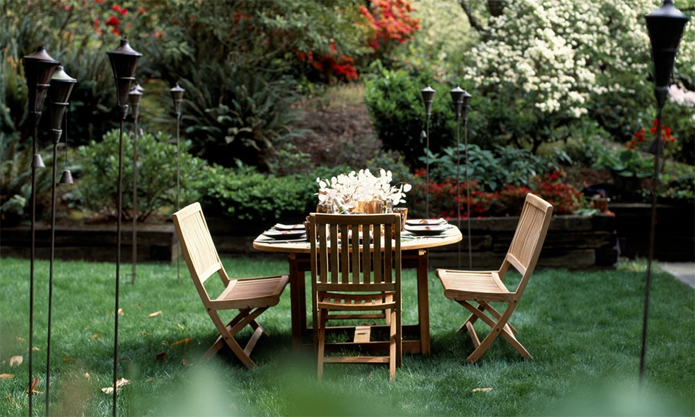 Eine mit Tellern und Blumen dekorierte Gartentischgarnitur steht in einem sorgfältig gestalteten kleinen Garten.