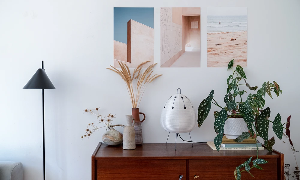 Ein Sideboard im Mid Century Interior Stil, dekoriert mit einer weißen Tischlampe, Vasen mit getrockneten Gräsern und einer Zimmerpflanze. 