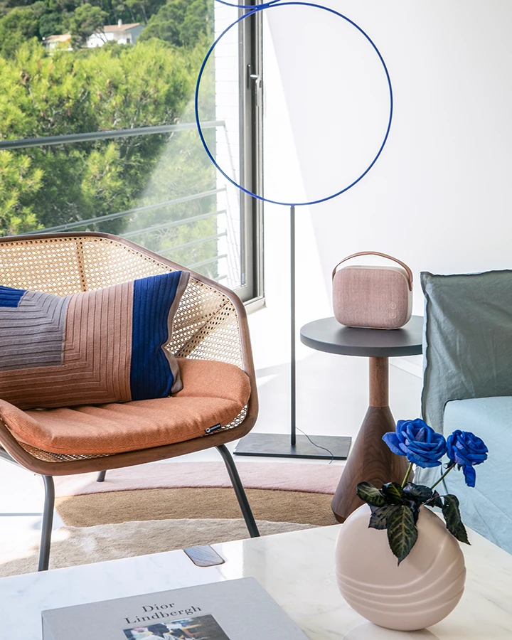 Ein heller Wohnbereich im Mid Century Interior Stil mit einem Rattansessel, der mit bunten Kissen dekoriert ist. 