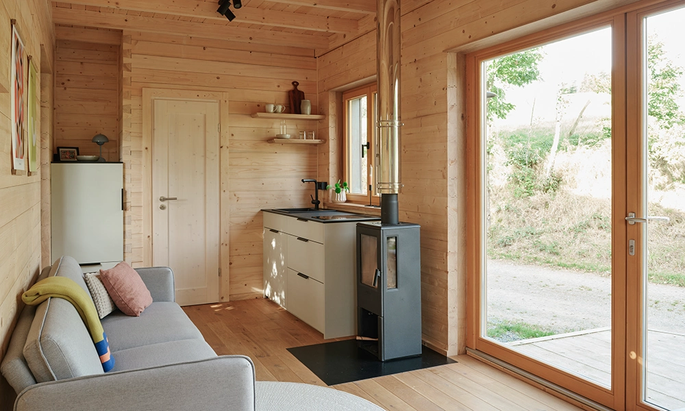 Das Innere eines Organic Tiny House zeigt eine kleine Küche und einen Kamin, umgeben von Holzwänden und -böden.