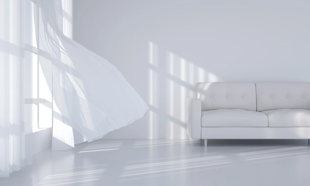 Ein helles Zimmer mit einem weißen Sofa und wehenden Vorhängen am Fenster, was an Schimmelsanierung denken lässt, da die Reinheit des Raumes betont wird.