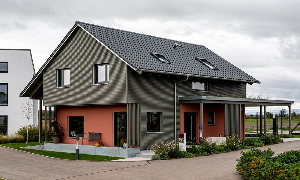 Ein modernes Einfamilienhaus Aenne mit einer Kombination aus grauer und orangefarbener Fassade, versehen mit einem Carport auf der Seite.