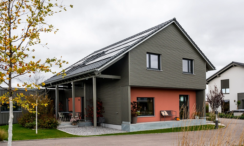 Ein modernes Fertighaus "Aenne" mit grauer Fassade und orangefarbenem Untergeschoss, das Solarpanelen auf dem Dach hat.