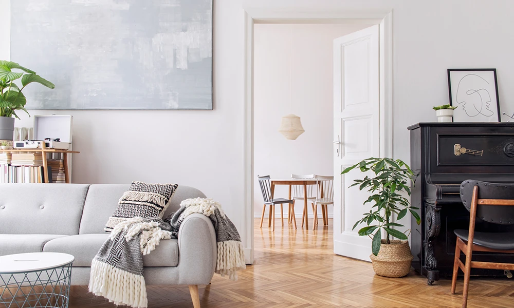 Helles Wohnzimmer im skandinavischen Wohnstil mit grauem Sofa, Holzboden, Pflanzen und minimalistischen Dekorationen.