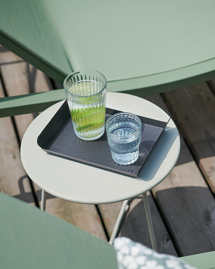 Elegant outdoor lounger and bistro table in mint green. Two crystal glasses with drinks are on the table. Spring-like atmosphere.