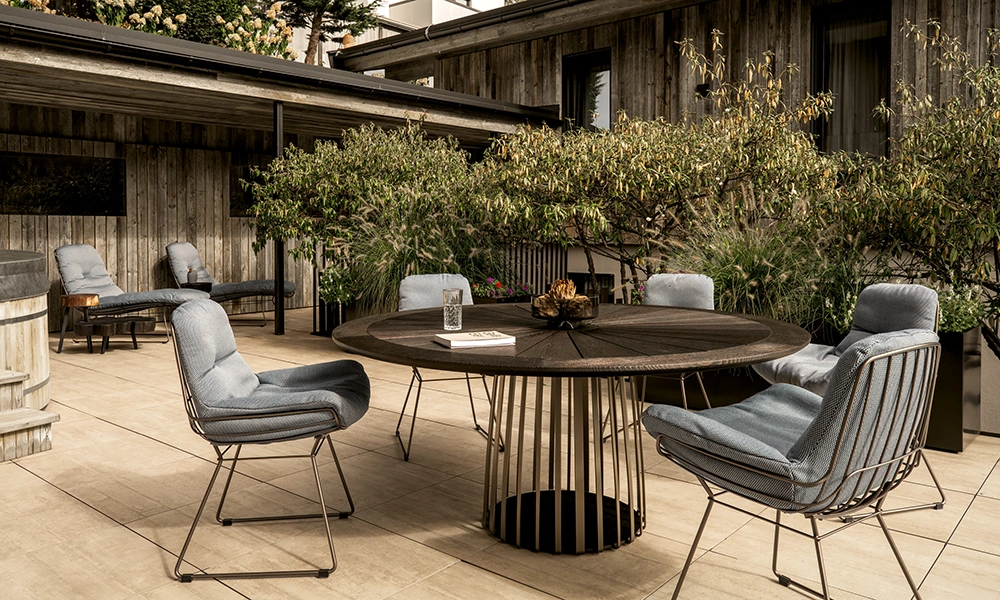 An inviting outdoor patio area in spring with comfortable seating and a rustic wooden table, surrounded by lush greenery.