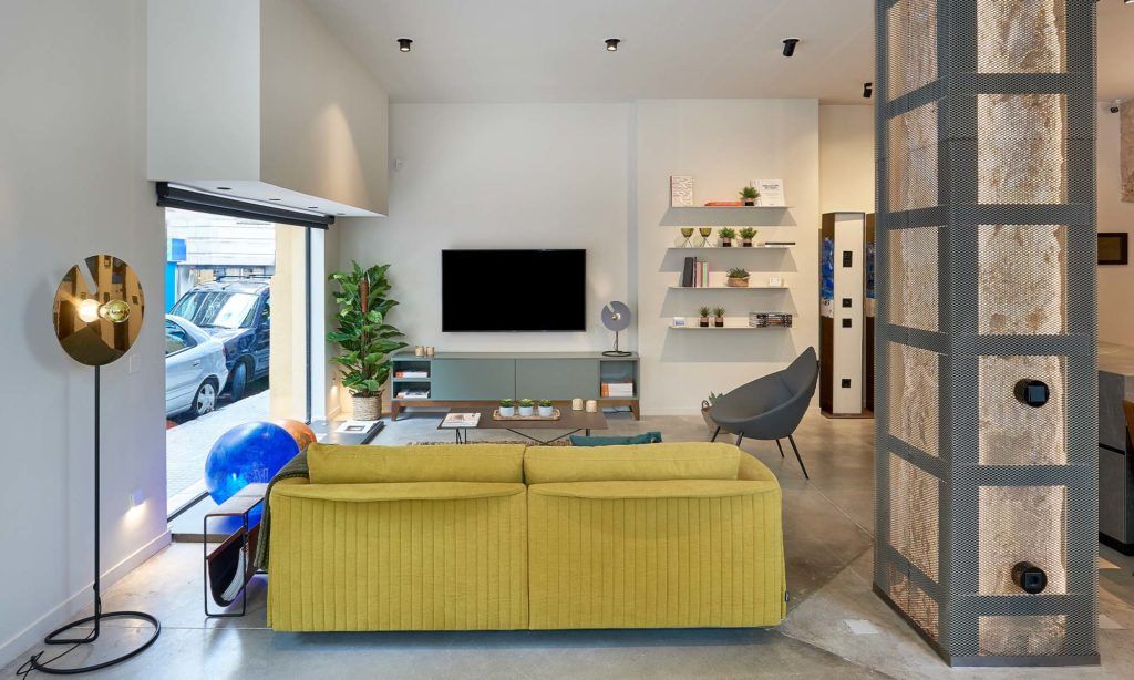 Gira showroom featuring a stylish living area with a yellow sofa, modern lighting, and a wall-mounted TV, showcasing contemporary home automation solutions.