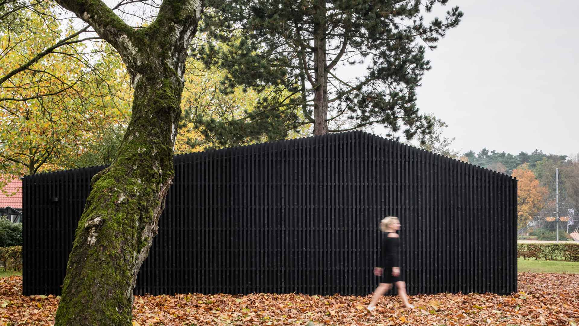 Black wooden house in nature with a woman walking in front of it